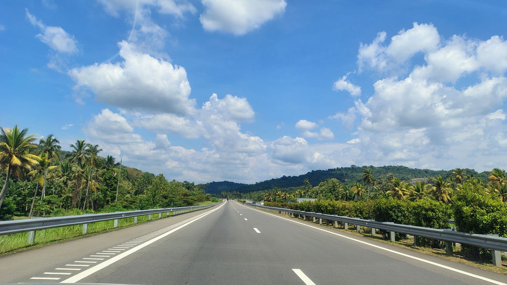 An expressway near Kurunegala, Sri Lanka, lined with coconut palms under a blue sky